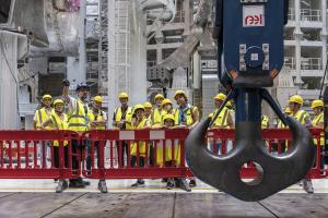 Lors d'une Journée Portes Ouvertes, vous pouvez visiter ITER en portant, comme les gens dans cette photo qui regardent un dispositif de levage, un gilet de sécurité jaunes et un casque.