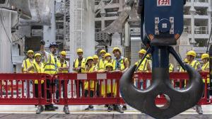 Lors d'une Journée Portes Ouvertes, vous pouvez visiter ITER en portant, comme les gens dans cette photo qui regardent un dispositif de levage, un gilet de sécurité jaunes et un casque.